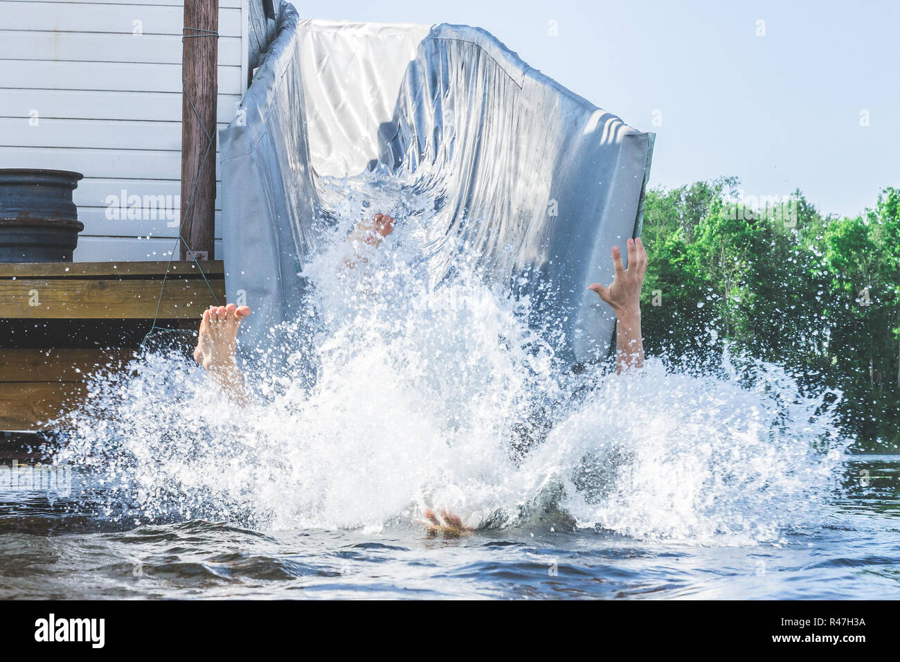 Le gambe e le braccia di una persona fuori di una enorme quantità di spruzzi d'acqua scende in estate sul lago. Divertente intrattenimento d'acqua. Foto Stock