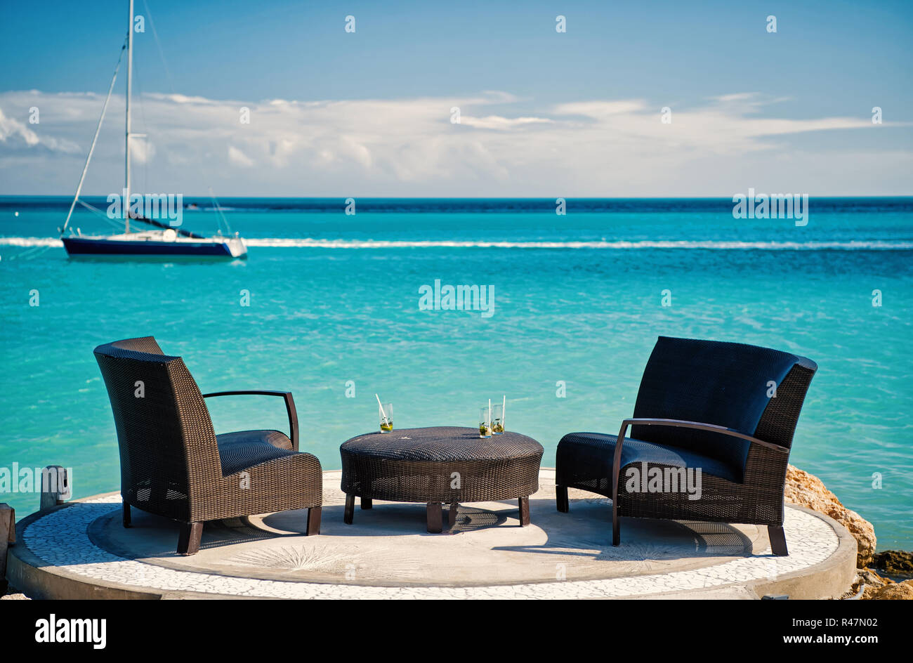 Poltrone e tavolo sulla spiaggia tropicale in st Johns, Antigua. Arredamento di rattan e yacht in mare turchese o acqua oceanica. Vacanze estive sui Caraibi. Foto Stock