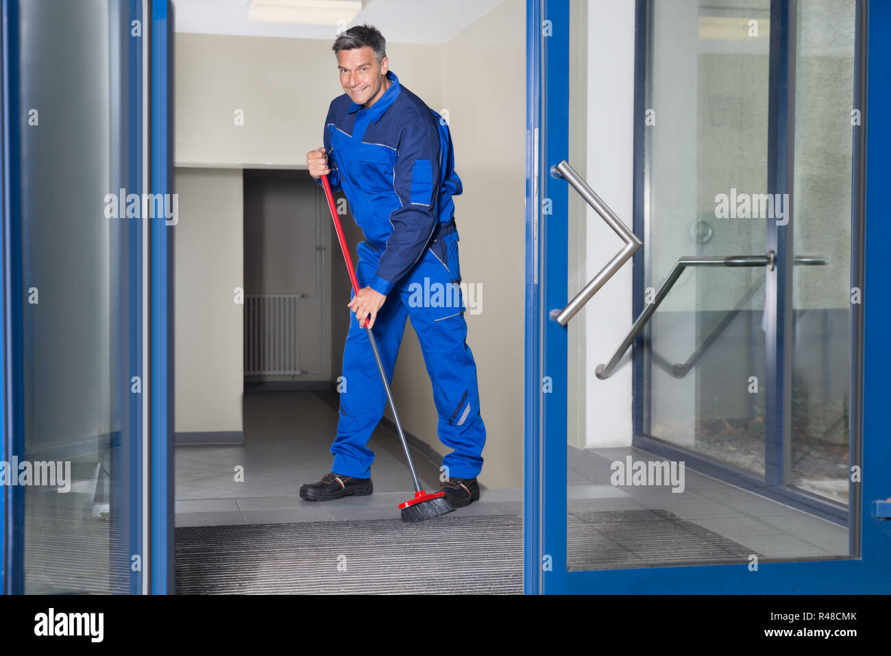 Fiducioso lavoratore matura scopa con pavimento di pulizia Foto Stock