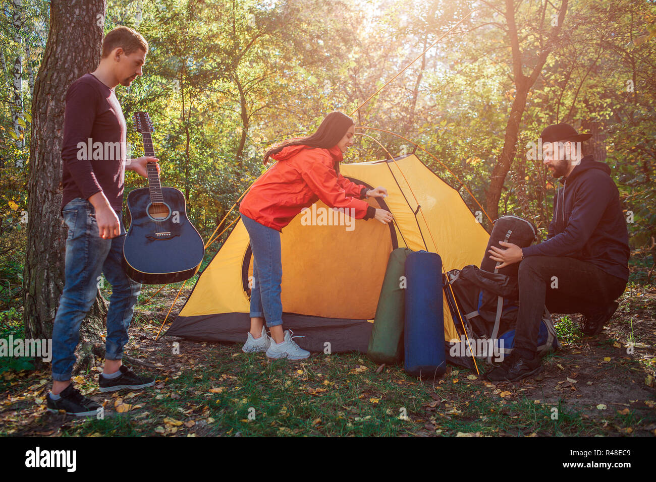 Bella e positiva giovane donna immettere di chiusura della tenda. Ragazzo sulla sinistra ha la chitarra in mani. Giovane uomo sulla destra si siede e si sacco a pelo fuori rocksack. Foto Stock