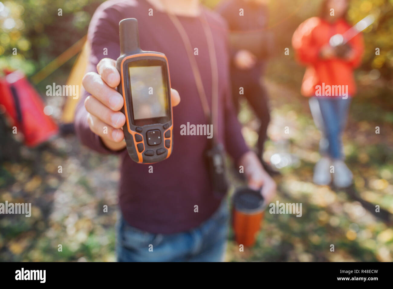 Immagine dell uomo con telefono satellitare e thermocup in mani. Egli mostra che la fotocamera. Giovane uomo e donna stanno dietro. Foto Stock
