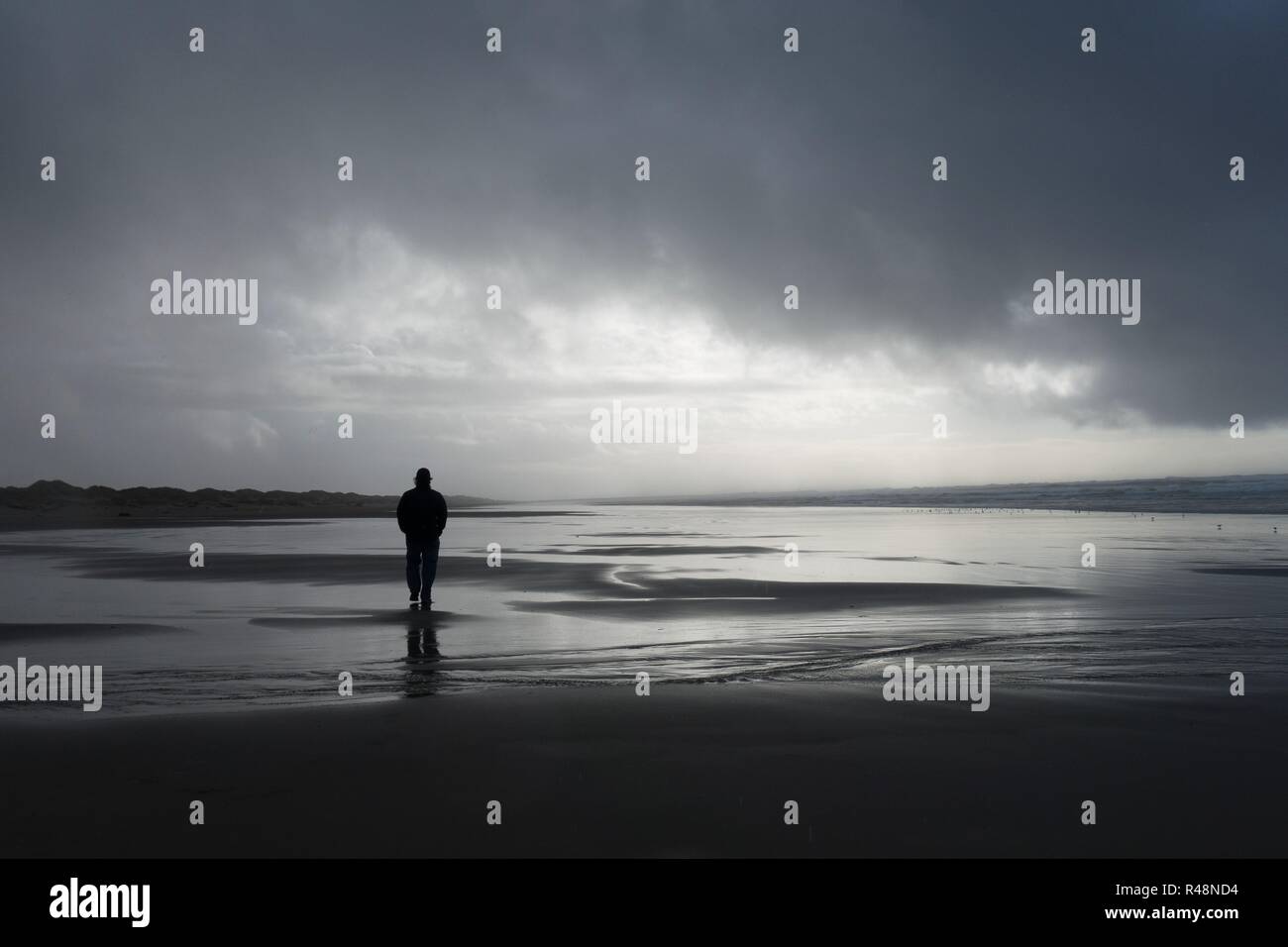 Silhouette di un uomo a piedi su una spiaggia sotto un cielo nuvoloso. Foto Stock