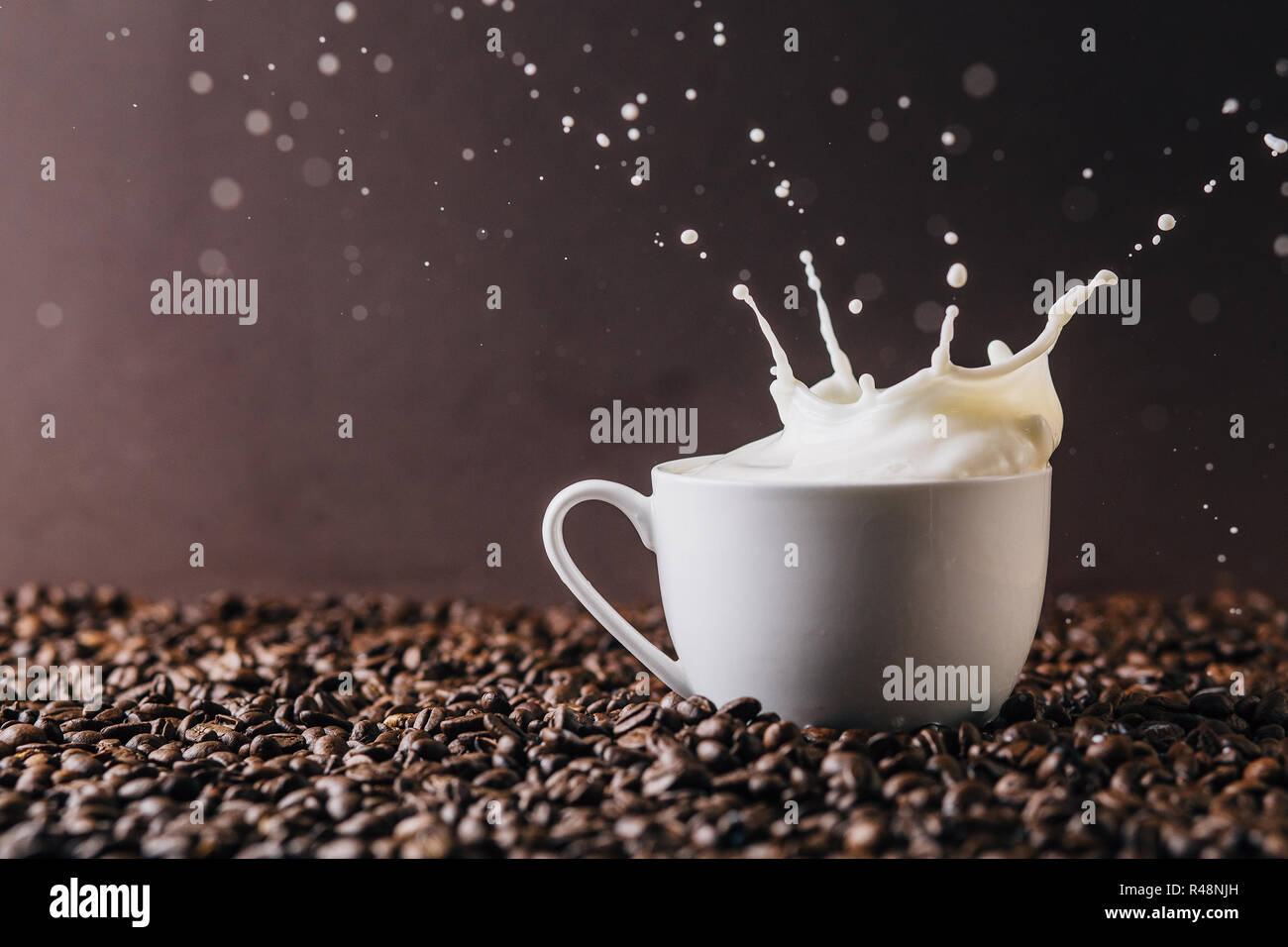 Una tazza di latte con schizzi sopra un tavolo ricoperto di chicchi di  caffè Foto stock - Alamy