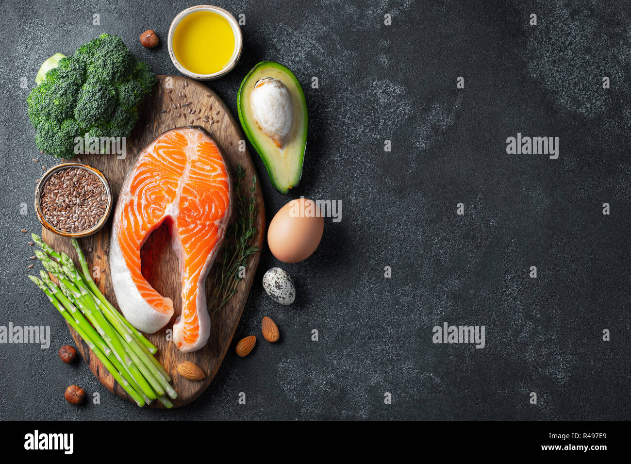 Un insieme di un alimento sano per il cheto dieta su uno sfondo scuro. Crudo fresco bistecca di salmone con semi di lino, broccoli, avocado, uova di gallina, dadi e gli asparagi Foto Stock