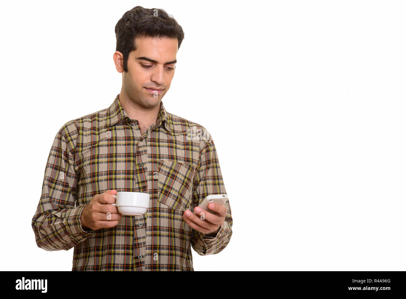Giovane uomo persiano utilizzando il telefono cellulare mentre si tiene tazza da caffè Foto Stock