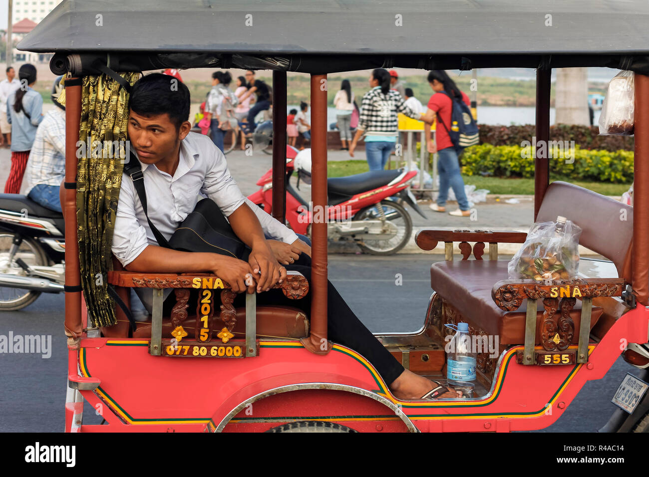 Remork-moto (moto & trasporto) driver su occupato riverfront al tramonto. Preah Sisowath Quay, centro della città di Phnom Penh, Cambogia Foto Stock