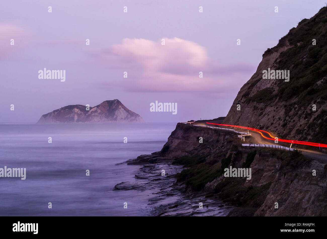 Luci rosse di una vettura guida su un telecomando East Cape strada costiera con telecomando isola, nebbia e ripida scogliera rendendo il paesaggio Foto Stock