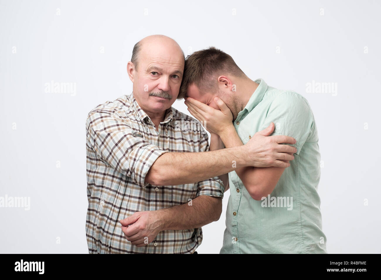 Coppia figlio piange sul suo padre lo spallamento e la sensazione di sconvolgere la causa di un suo errore. Foto Stock
