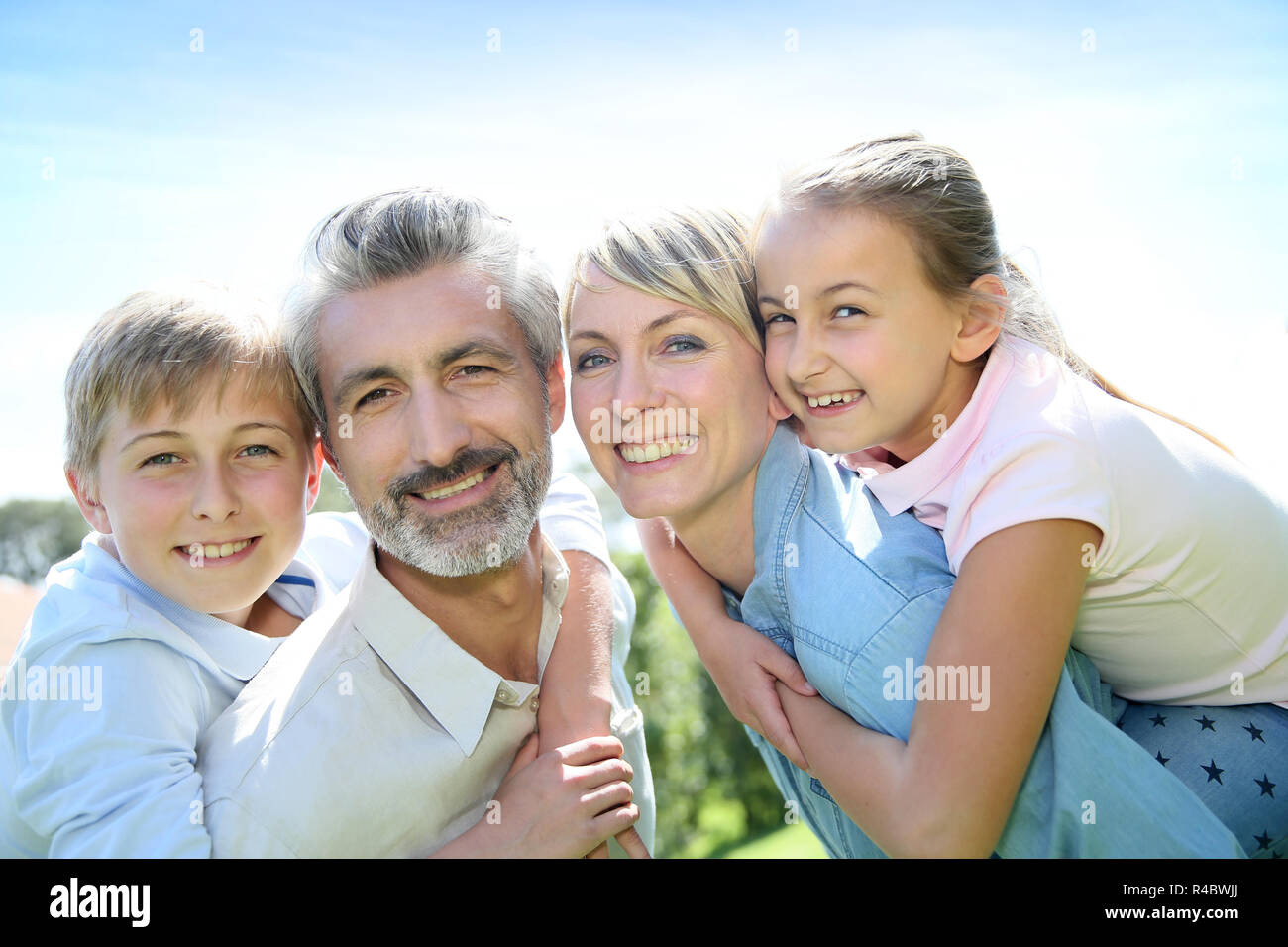 I genitori dando piggyback ride per i bambini in giardino Foto Stock