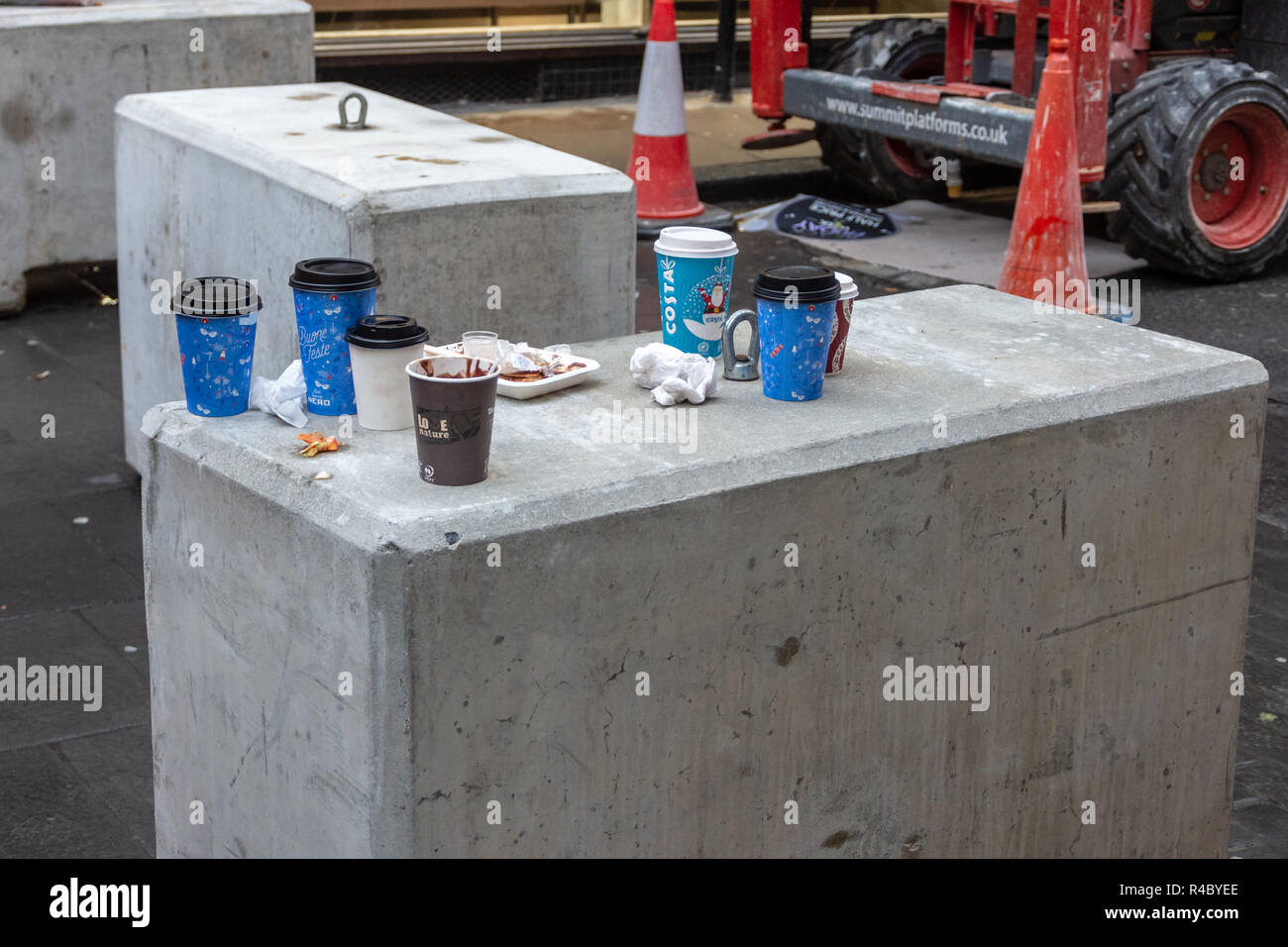 Scartato festosa costa tazze monouso e confezioni di cibo lasciato come lettiera su un blocco di cemento armato nella parte anteriore dei coni e dei macchinari da lavoro di costruzione Foto Stock