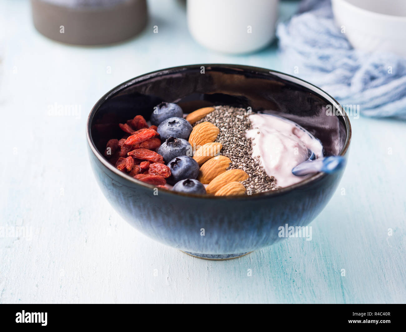 Frullato di yogurt ciotola con frutti di bosco, dadi, chia semi sul turchese pastello sullo sfondo di legno. Impianto basato vegane prima colazione Foto Stock