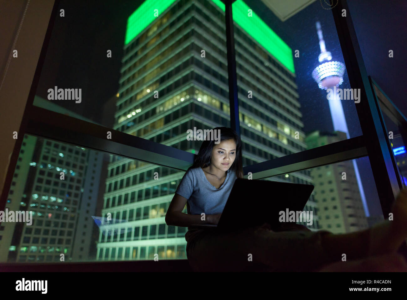 Giovane bella donna asiatica utilizzando laptop contro il vetro della finestra wi Foto Stock
