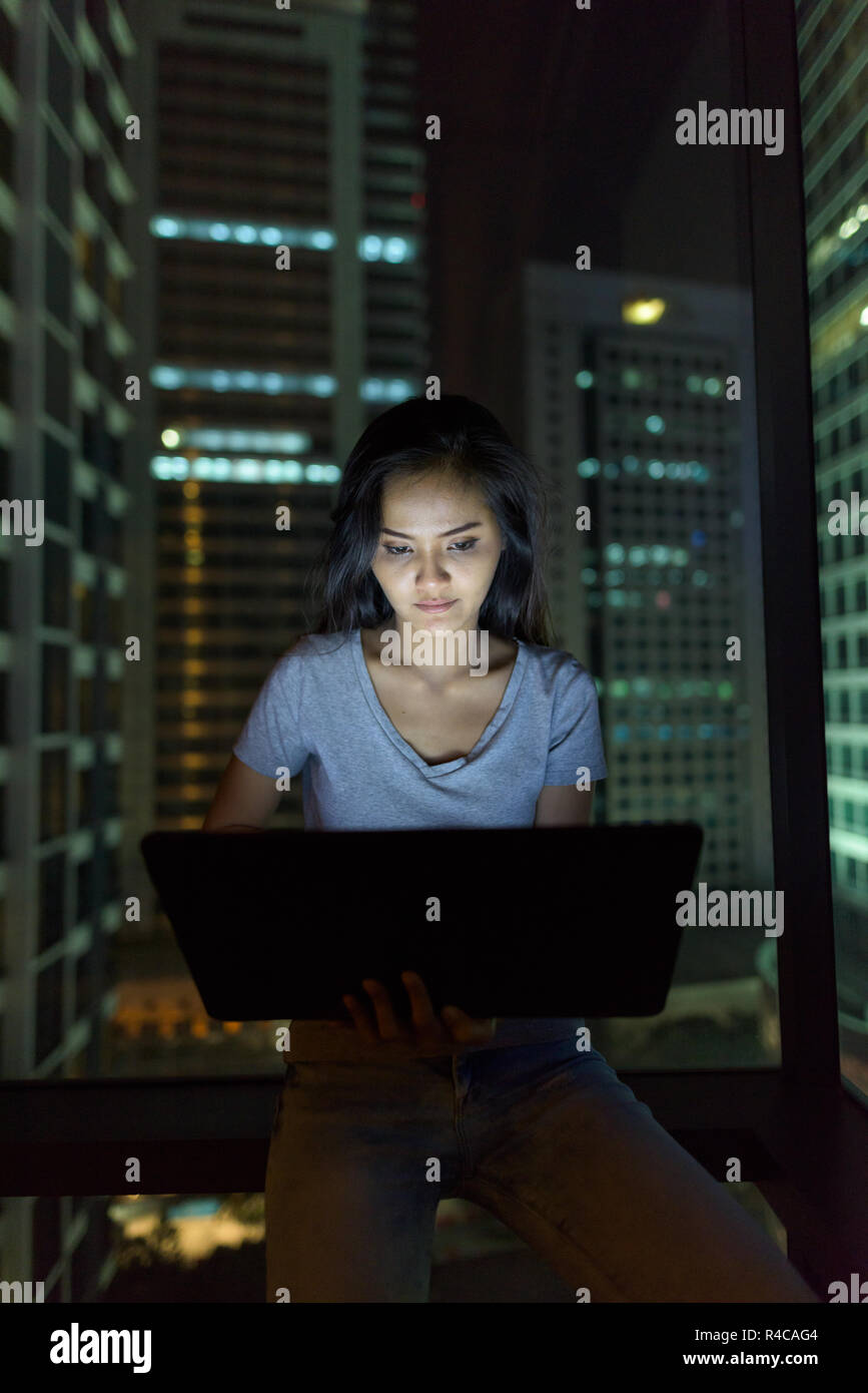 Giovane bella donna asiatica utilizzando laptop contro il vetro della finestra wi Foto Stock