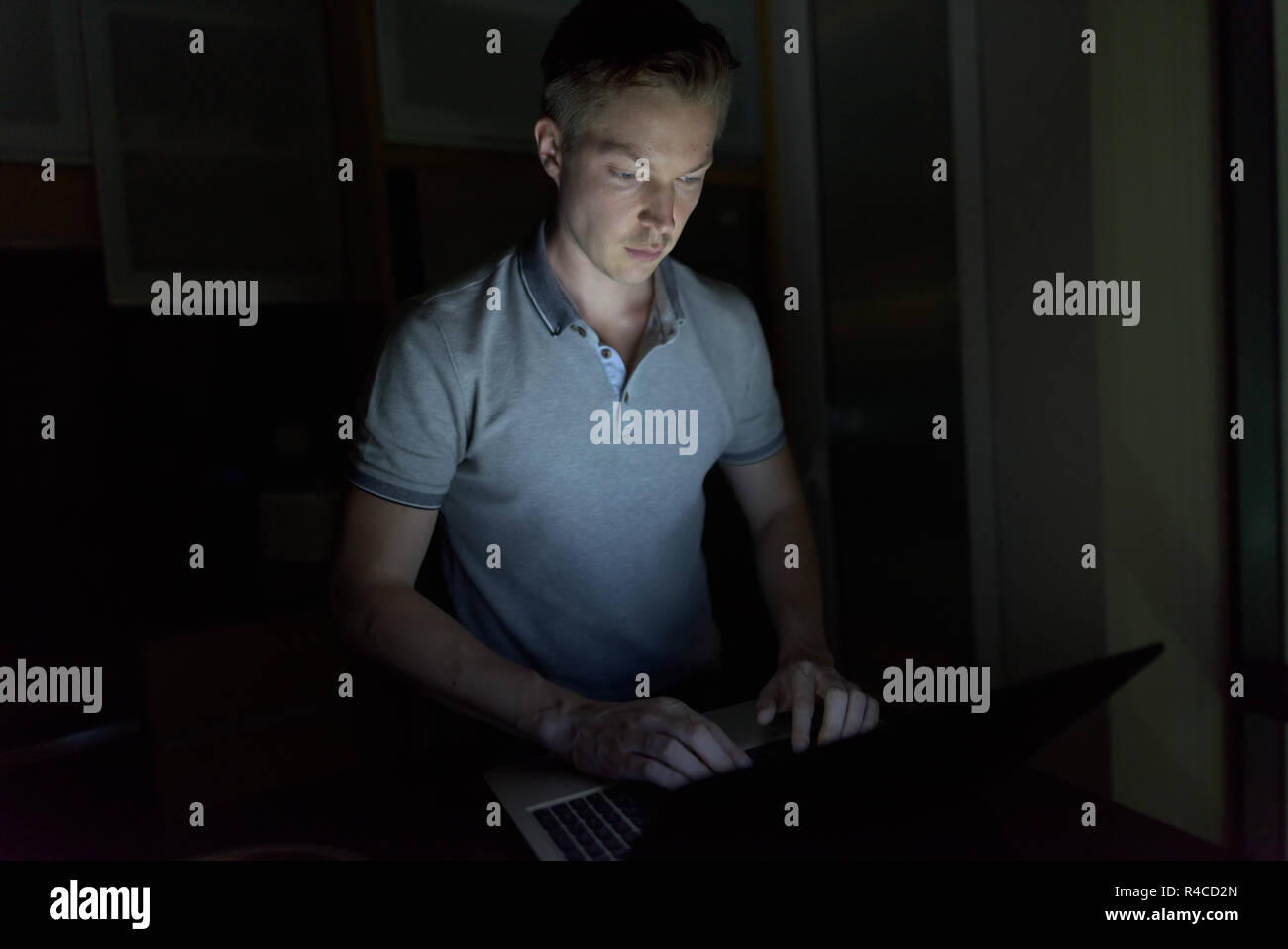 Giovane uomo bello utilizzando laptop nel buio soggiorno Foto Stock