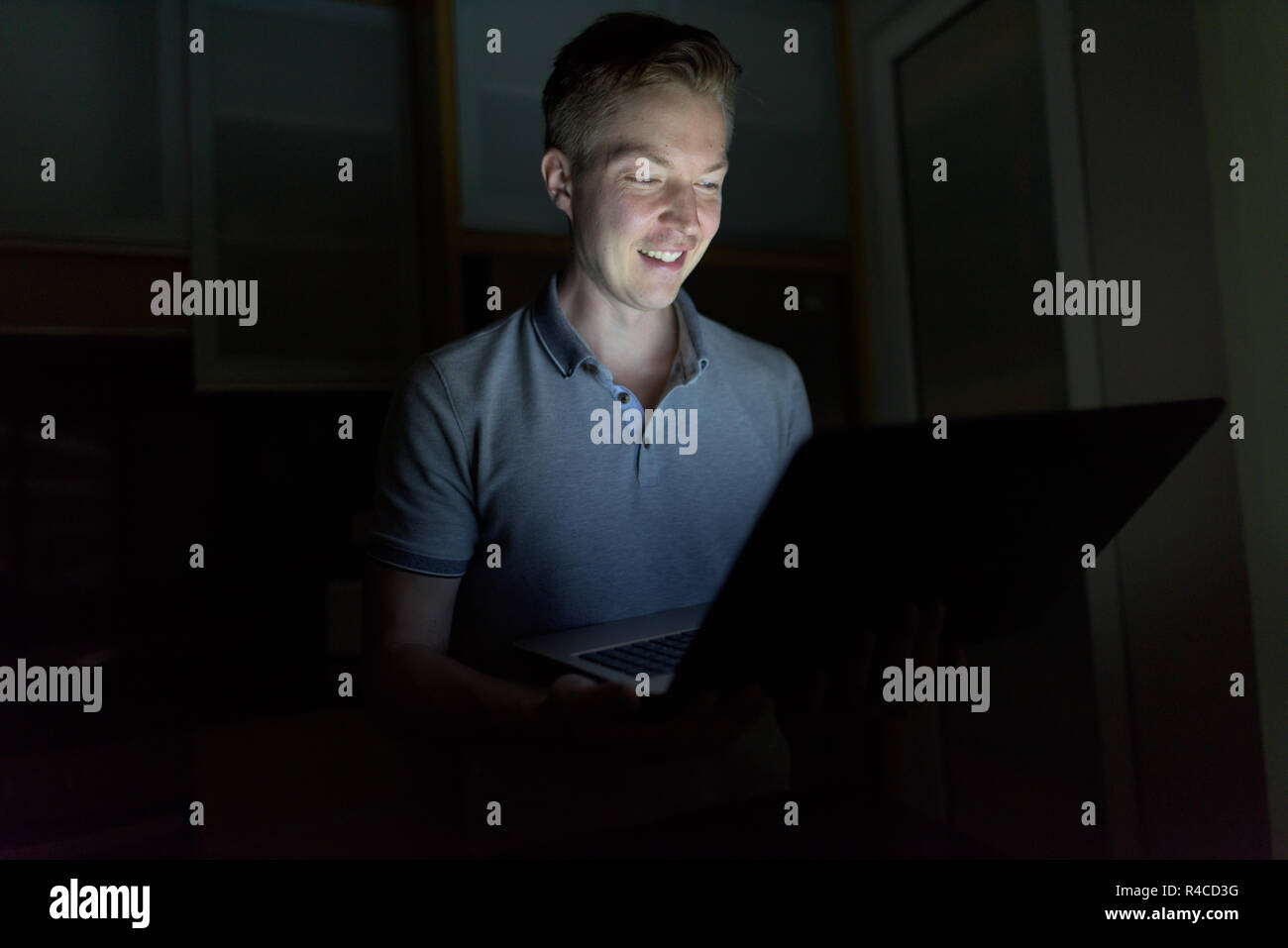 Giovane uomo bello utilizzando laptop nel buio soggiorno Foto Stock