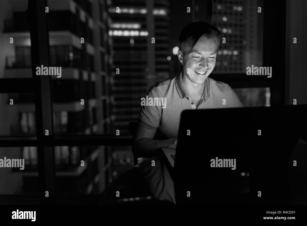 Giovane uomo bello utilizzando laptop contro la vista della città alla vicina Foto Stock