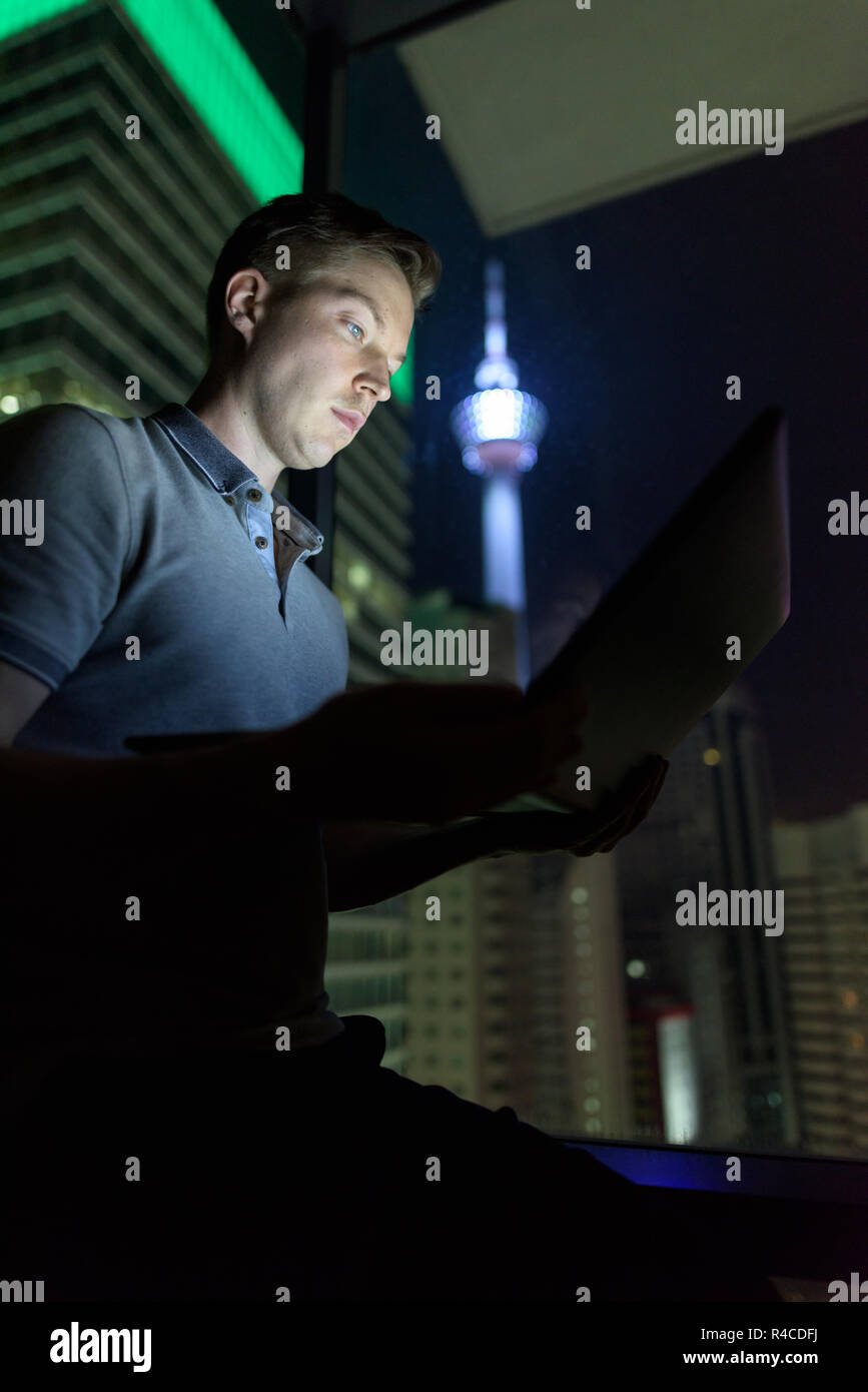 Giovane uomo bello utilizzando laptop contro il vetro della finestra con vista o Foto Stock