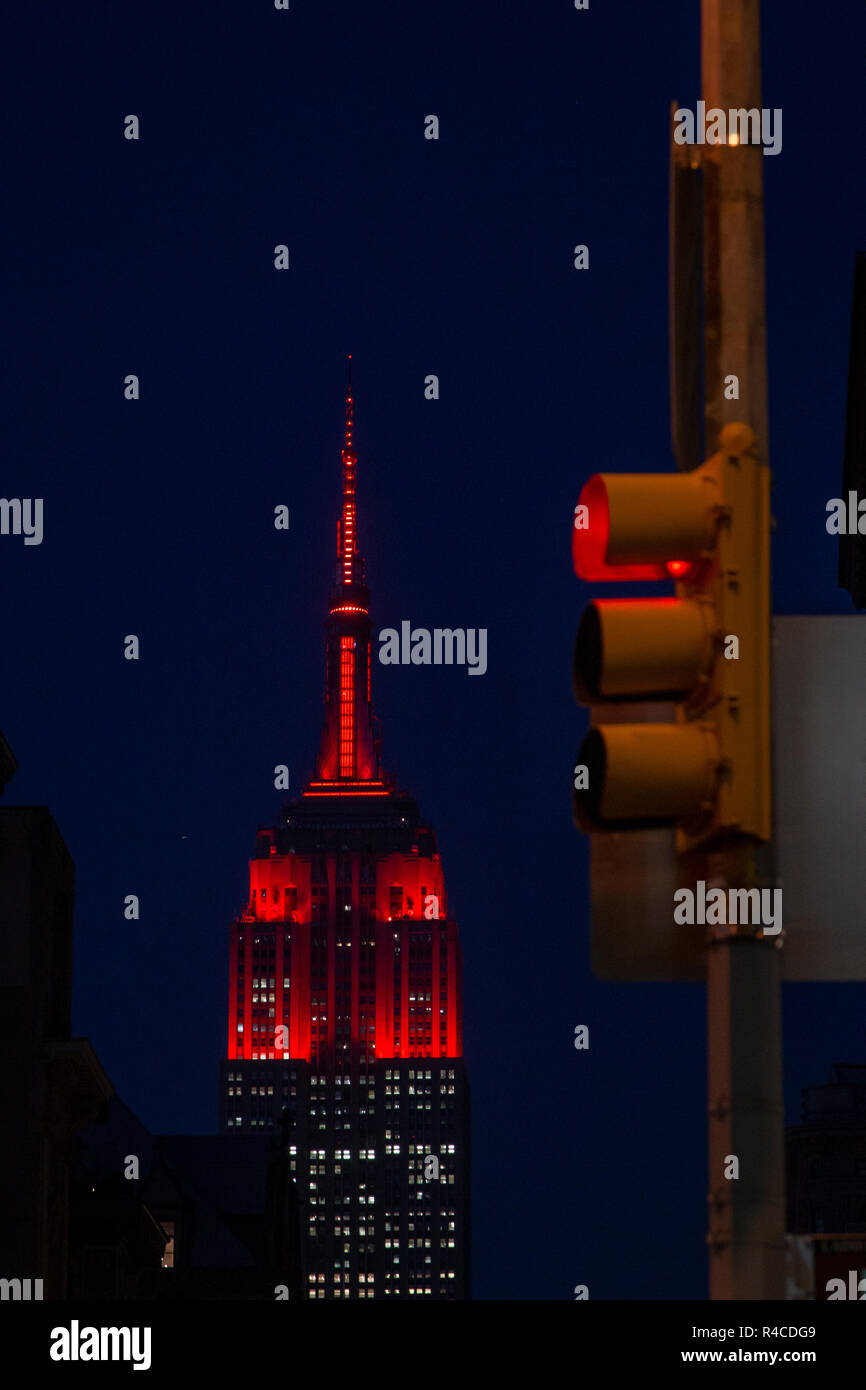 Un semaforo rosso in primo piano, mentre l'ESB Empire state Building è illuminato in rosso o in marrone. Il colore della ESB era quello di commemorare l'Università di Fordham 175 anni anniversario. Foto Stock