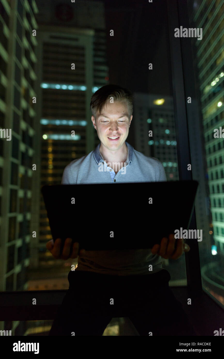 Giovane uomo bello utilizzando laptop contro il vetro della finestra con vista o Foto Stock