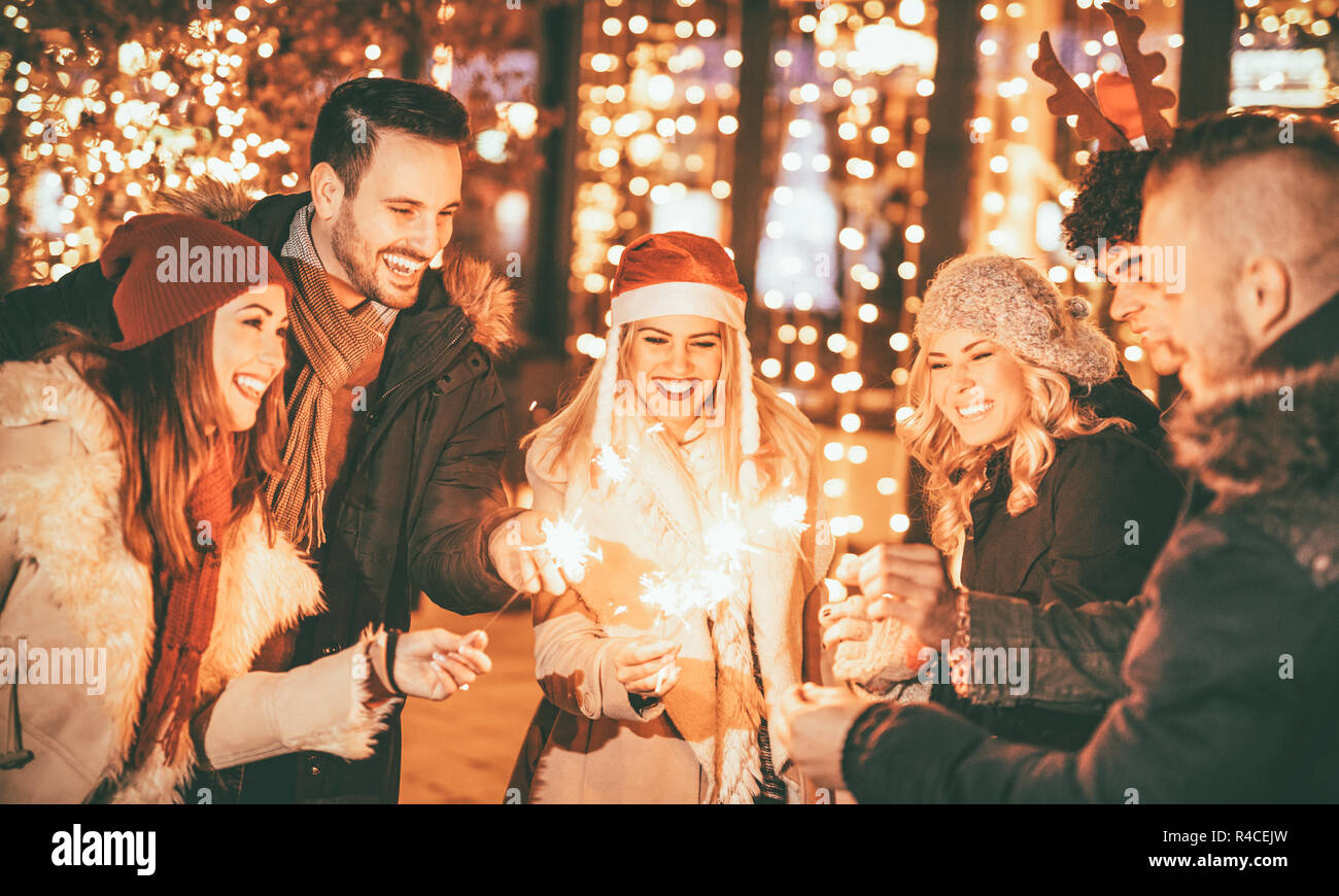 Un gruppo di giovani amici di Capodanno con bastoncini di scintilla divertirsi nella città Street di fronte luminosa finestra del negozio. Foto Stock