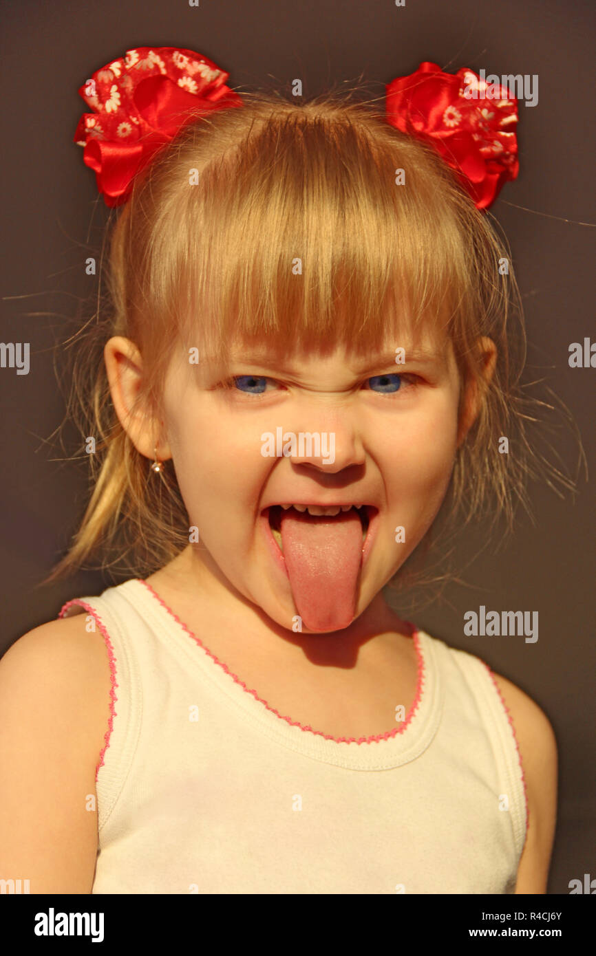 Bambina mostra la linguetta. Ritratto di bambino sorride mostrando la sua lingua in divertenti centine rosso. Infanzia è il miglior tempo. Bambino felice Foto Stock