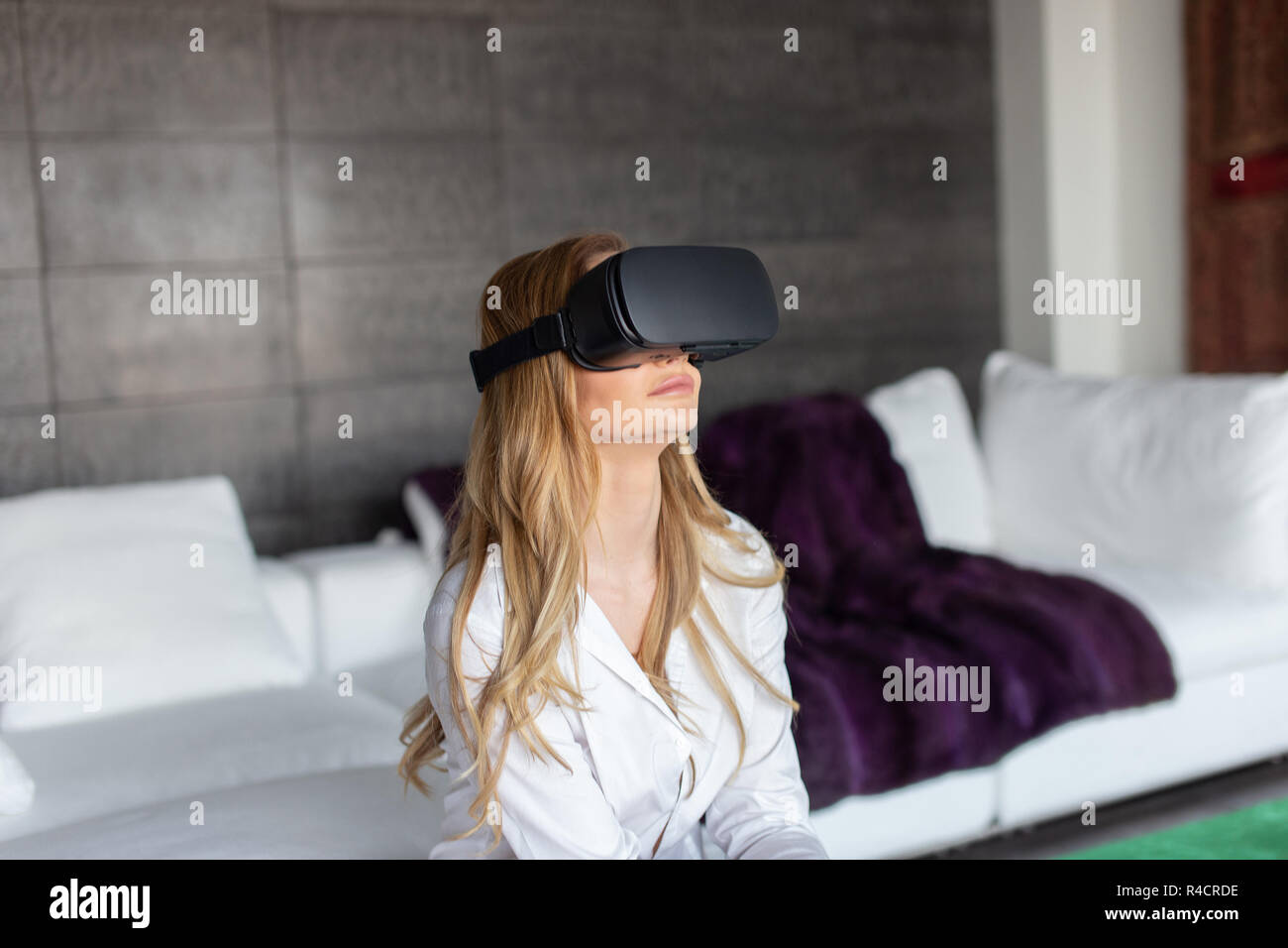 Giovane donna bionda con auricolare VR a casa, realtà virtuale Foto Stock