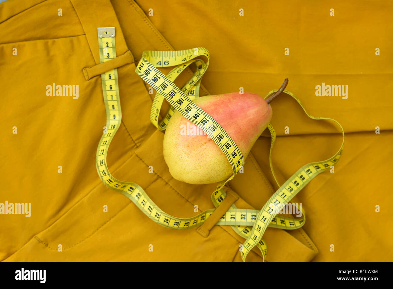 Giallo maturo pera e nastro di misurazione su sfondo giallo di pantaloni, uno stile di vita sano, sovrappeso e perdita di peso Foto Stock