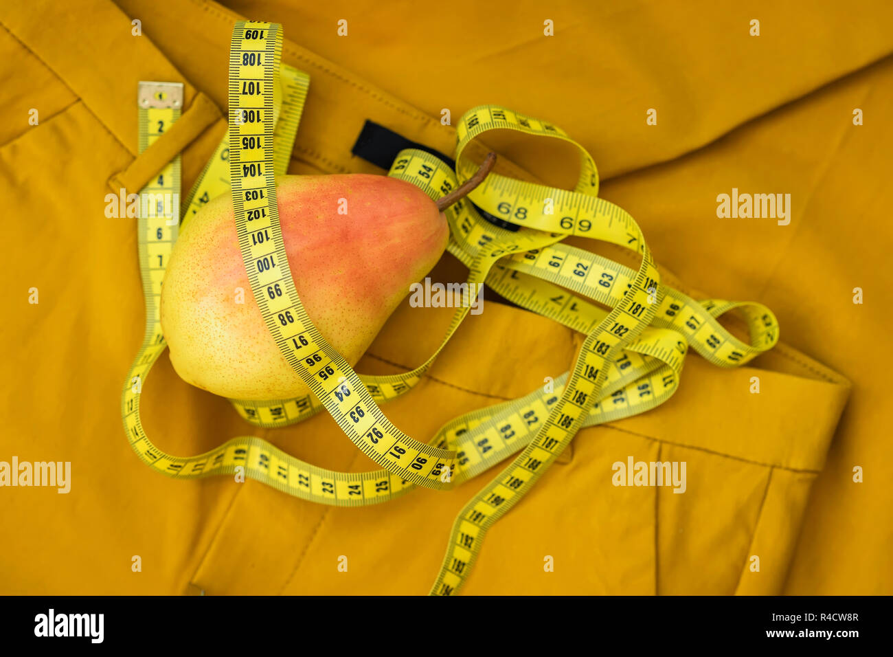 Pera matura e nastro di misurazione su sfondo giallo di pantaloni, il concetto di uno stile di vita sano, dieta, il controllo del peso Foto Stock
