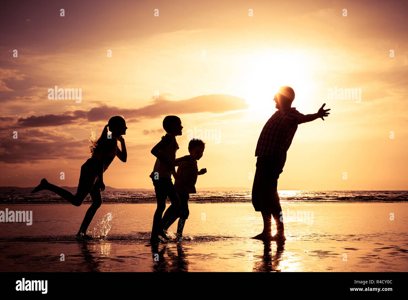 Padre e figli giocando sulla spiaggia al tramonto. Foto Stock