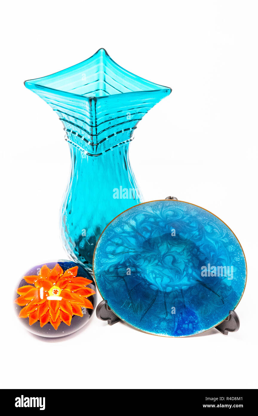 Un blu vaso di vetro e la piastra contro uno sfondo bianco con un fiore di arancia fermacarte in vetro. Foto Stock