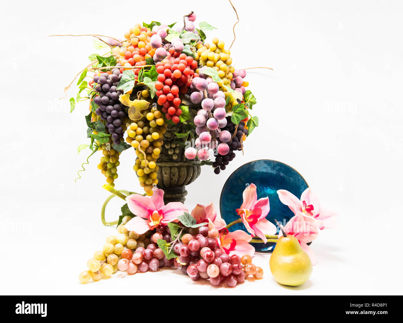 A colori a contrasto elevato ancora vita delle uve in un vaso di fronte a fiori, una pera e una lastra di vetro. Foto Stock