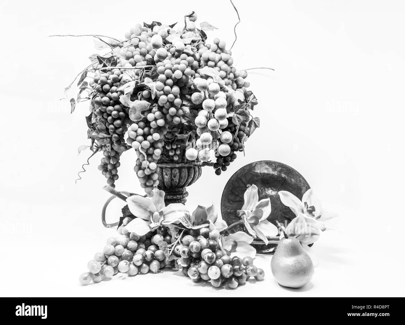 Alto contrasto bianco e nero ancora in vita di uve in un vaso di fronte a fiori e una lastra di vetro. Foto Stock