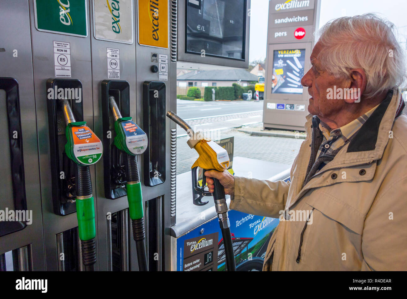 Uomo anziano scelta del carburante diesel ugello della pompa e la visione di caro prezzo al distributore di carburante di gas stazione per il rifornimento di carburante la sua auto in Belgio, Europa Foto Stock