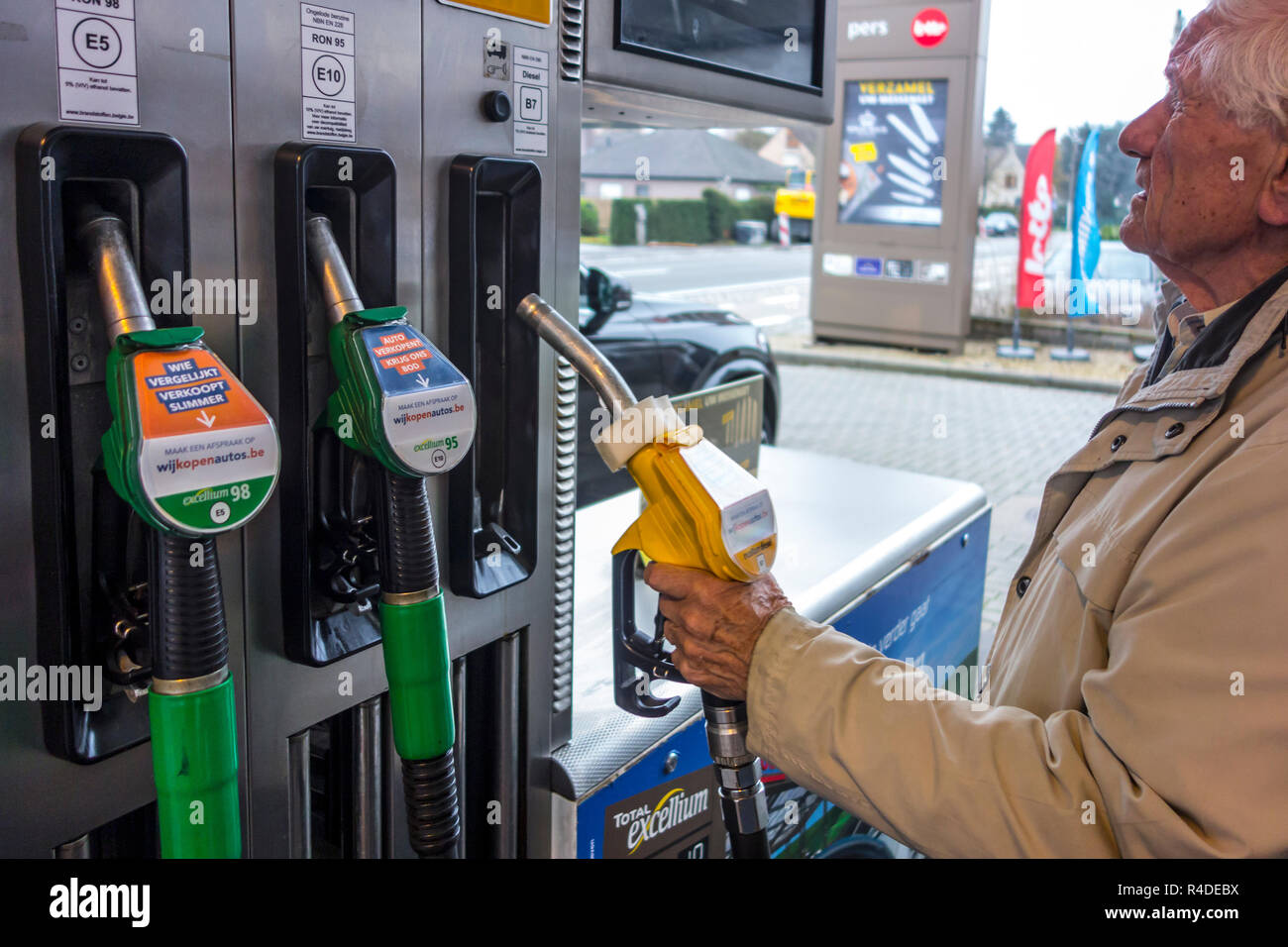 Uomo anziano scelta del carburante diesel ugello della pompa e la visione di caro prezzo al distributore di carburante di gas stazione per il rifornimento di carburante la sua auto in Belgio, Europa Foto Stock
