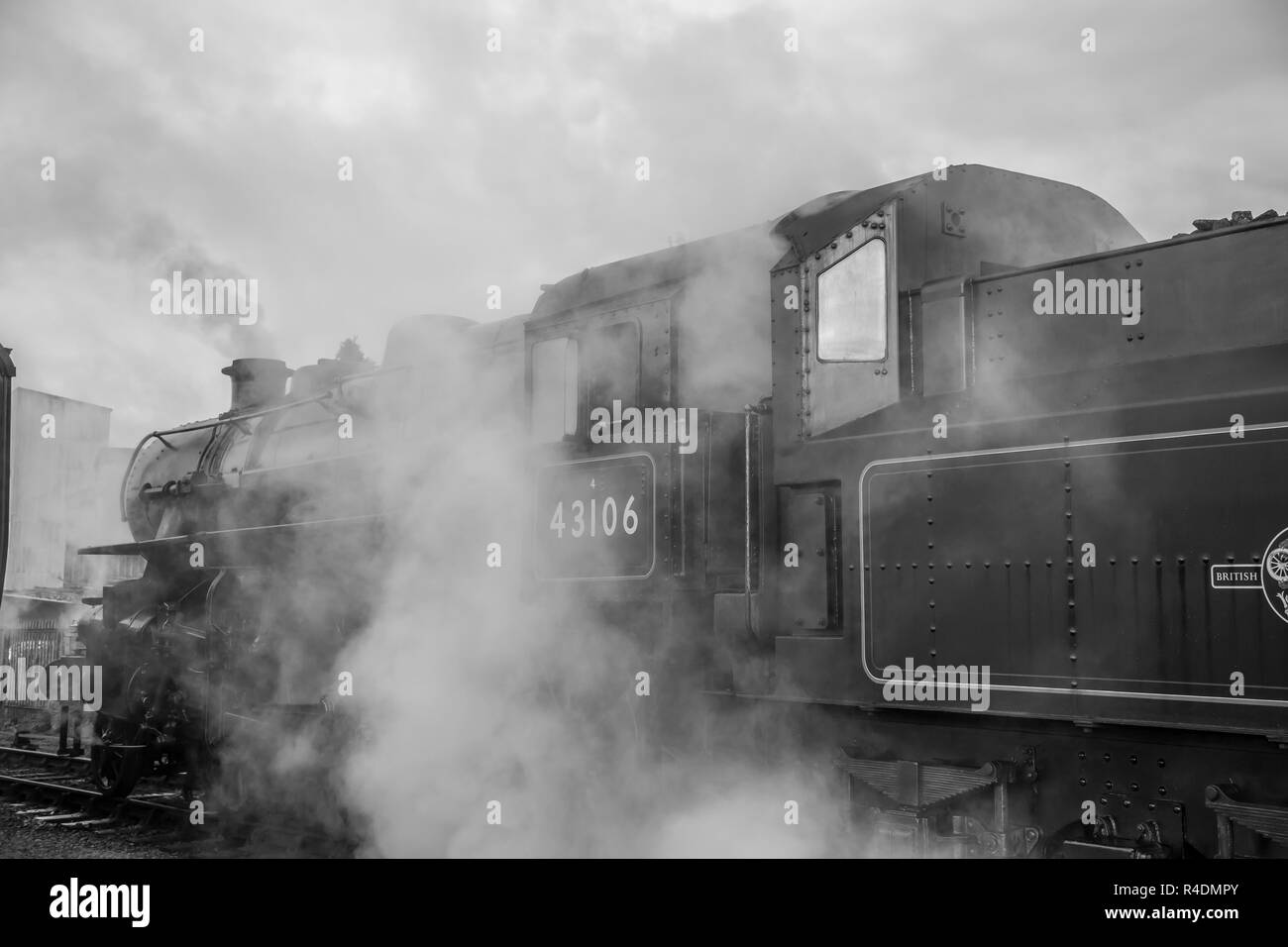 Bianco e nero, atmosfera, vista laterale da vicino della vecchia locomotiva a vapore del Regno Unito d'epoca in attesa della partenza, accanto alla piattaforma, che rilascia vapore. Foto Stock