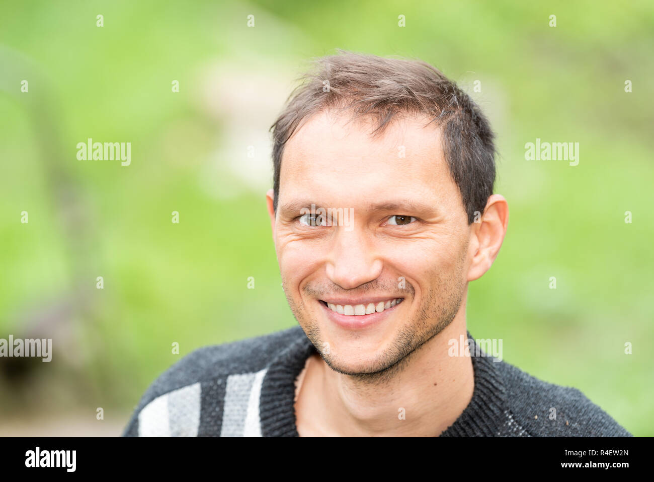 Giovane bello attraente uomo felice faccia closeup con stoppie, che mostra denti contadino nel giardino verde estate ritratto di sfondo Foto Stock