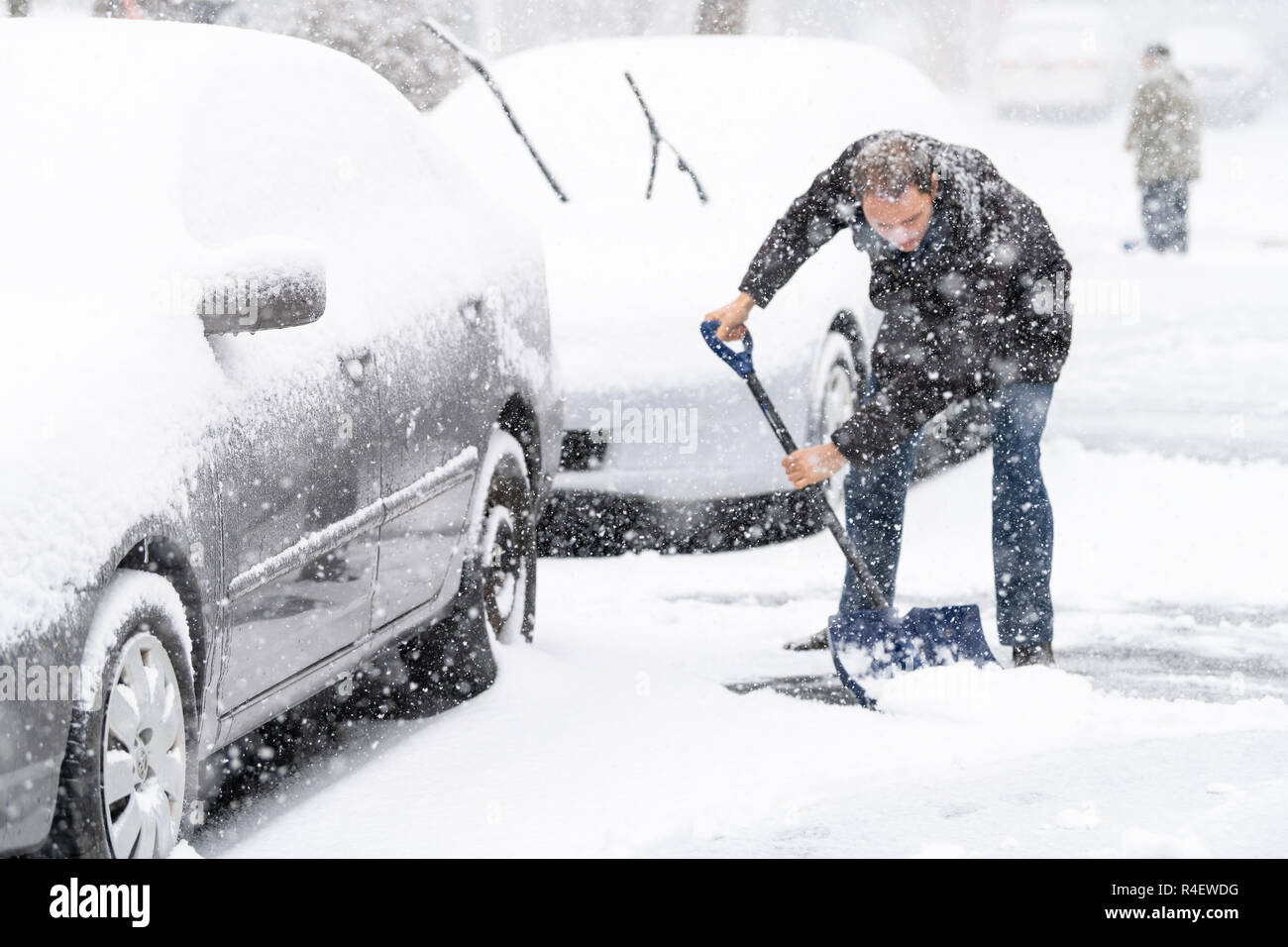 Giovane uomo, maschio in cappotto invernale pulizia, spalare carraio, strada coperta dalla caduta di neve in nevicata pesante tempesta di neve con la pala, residenziale hou Foto Stock