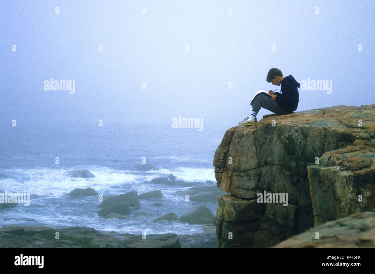 Un giovane ragazzo iscritto sulle rocce del Parco Nazionale di Acadia, Maine, Stati Uniti d'America Foto Stock