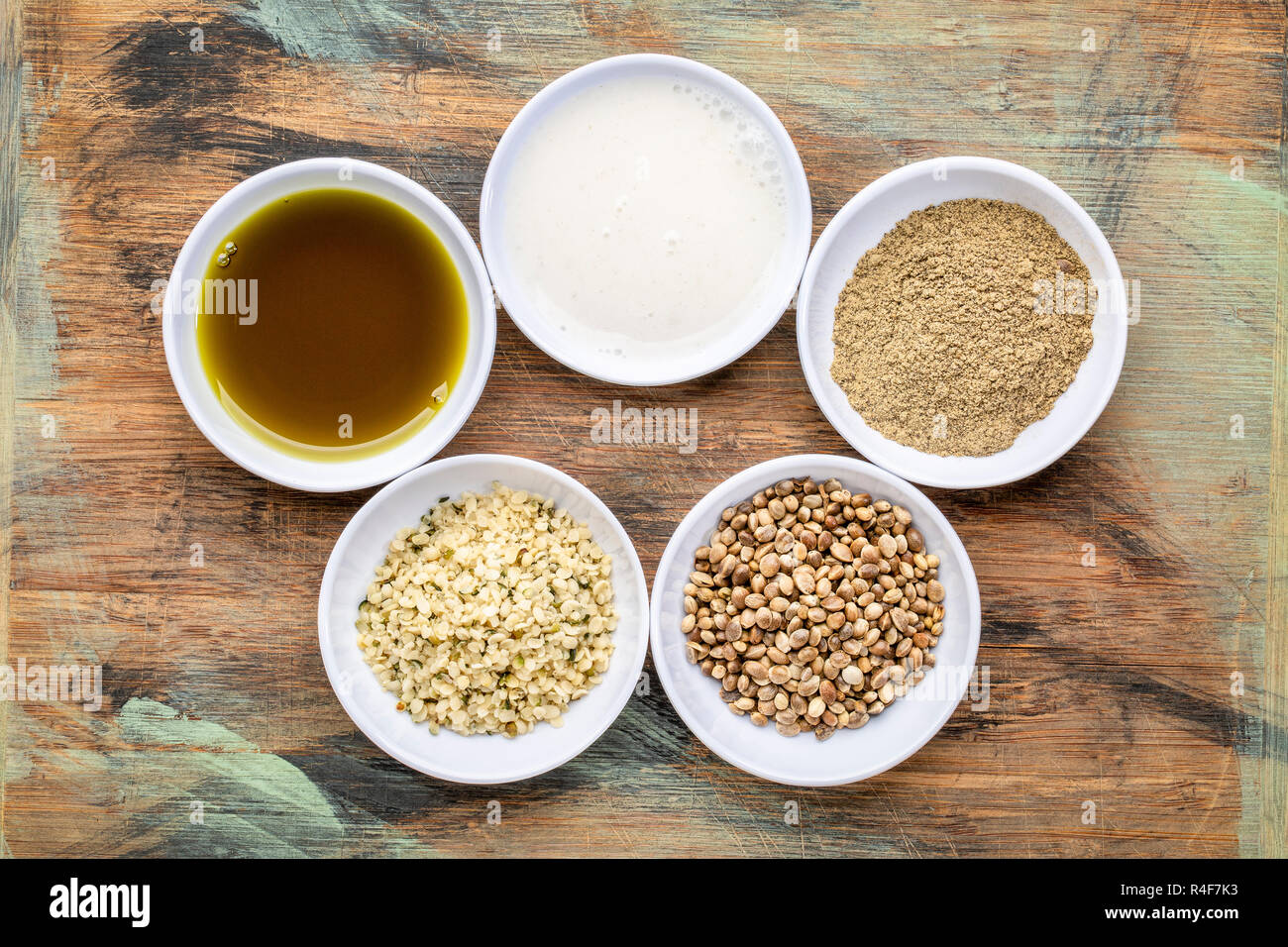 La raccolta di semi di canapa prodotto:s cuori, proteine in polvere, latte e olio in piccole ciotole bianco contro legno grunge Foto Stock