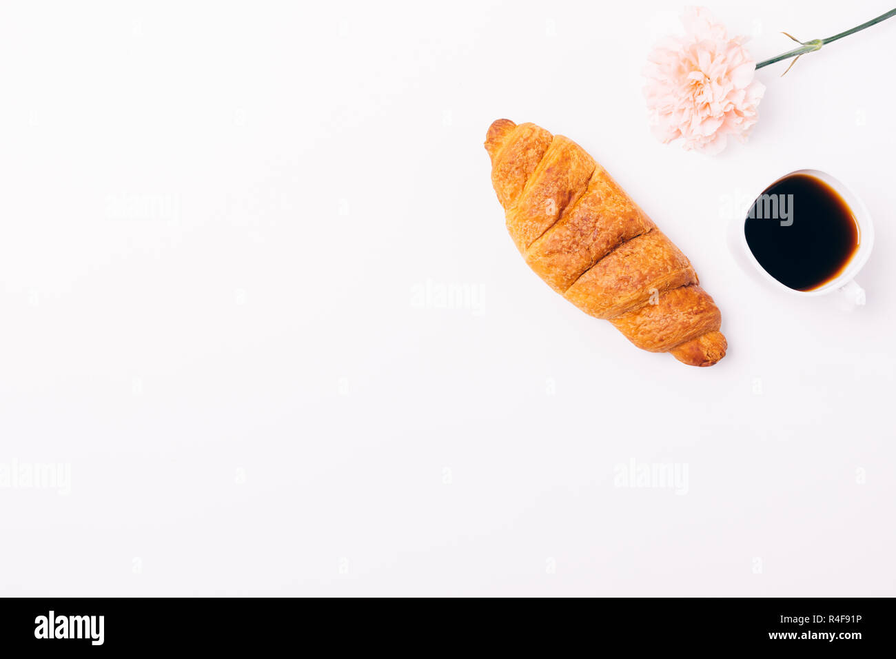 Croissant, una tazza di caffè nero e luce delicata fiore rosa su sfondo bianco con copia spazio, vista dall'alto. Foto Stock