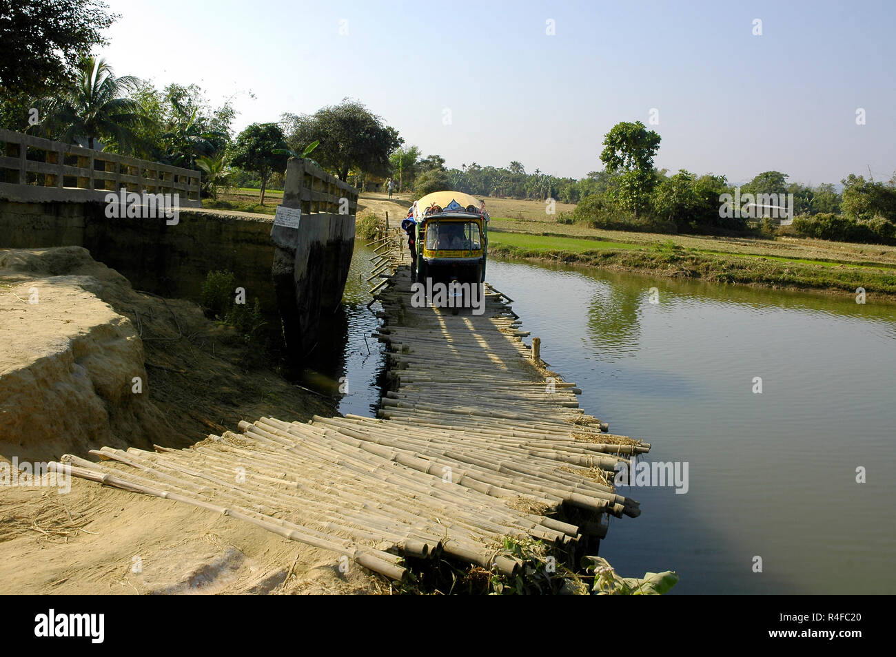 Una tre wheeler taxi attraversando un bambù fatti ponte di fortuna a Durgapur. Netrokona, Bangladesh. Foto Stock
