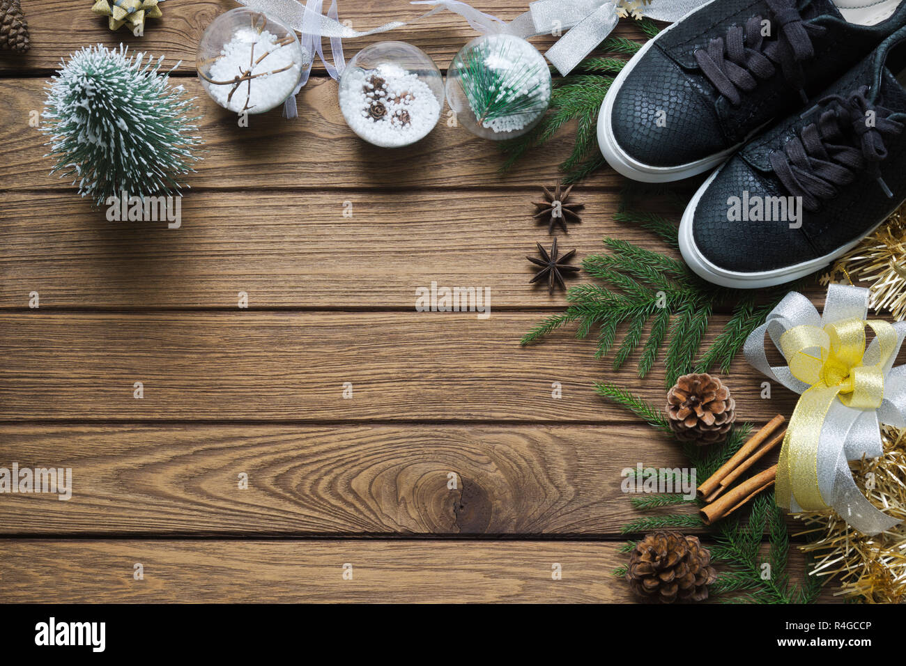 Piatto nero laici sneaker, mini albero di natale, oro e argento fiocchi, ornamenti Natale su uno sfondo di legno, Buon Natale di moda il concetto di sfondo. Foto Stock