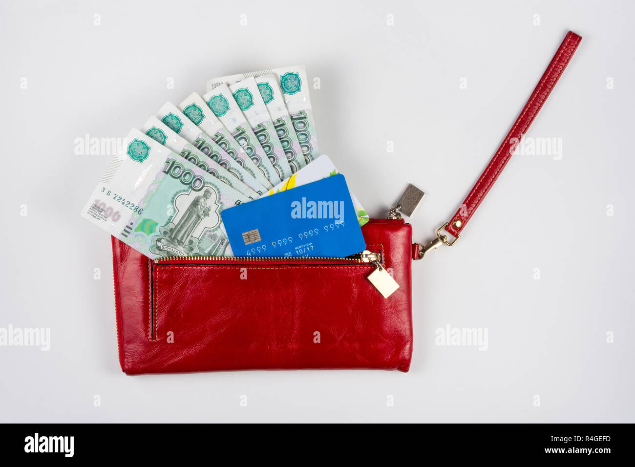 Portamonete rosso da cui fuoriesce il denaro e le carte di credito su sfondo bianco Foto Stock