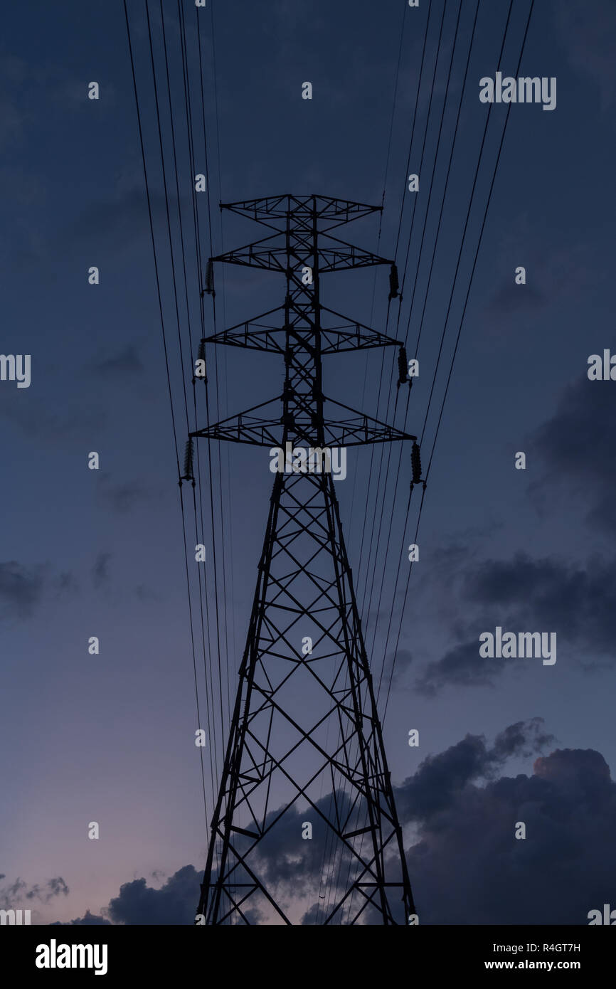 La trasmissione di energia elettrica ad alta tensione pilone silhouette con impianto di alimentazione contro dark lights sky. Foto Stock