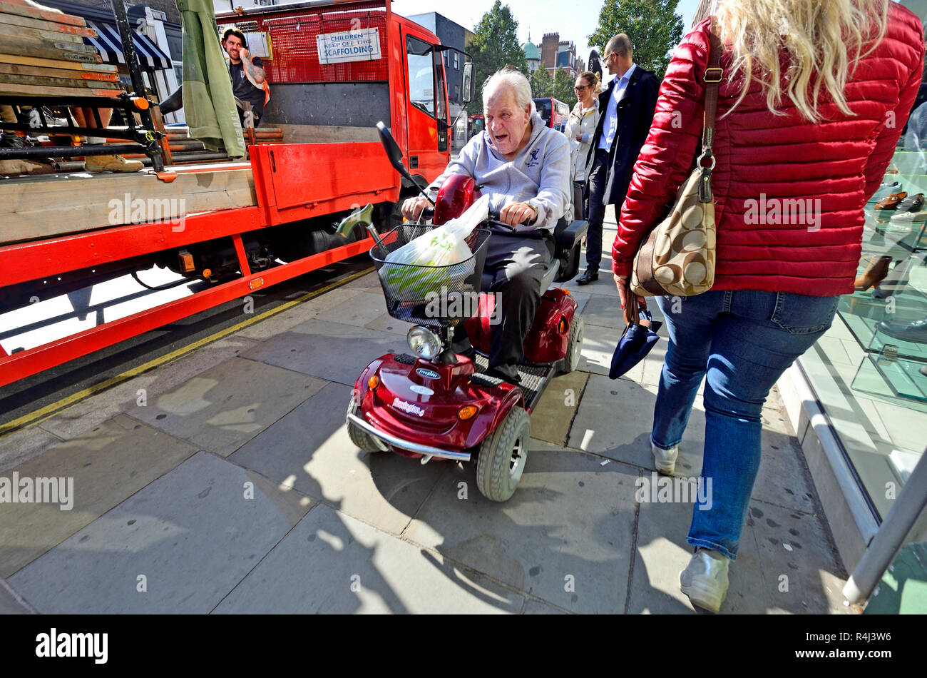 Uomo alla guida di una mobilità scooter sul marciapiede in centro a Londra, Inghilterra, Regno Unito. Foto Stock