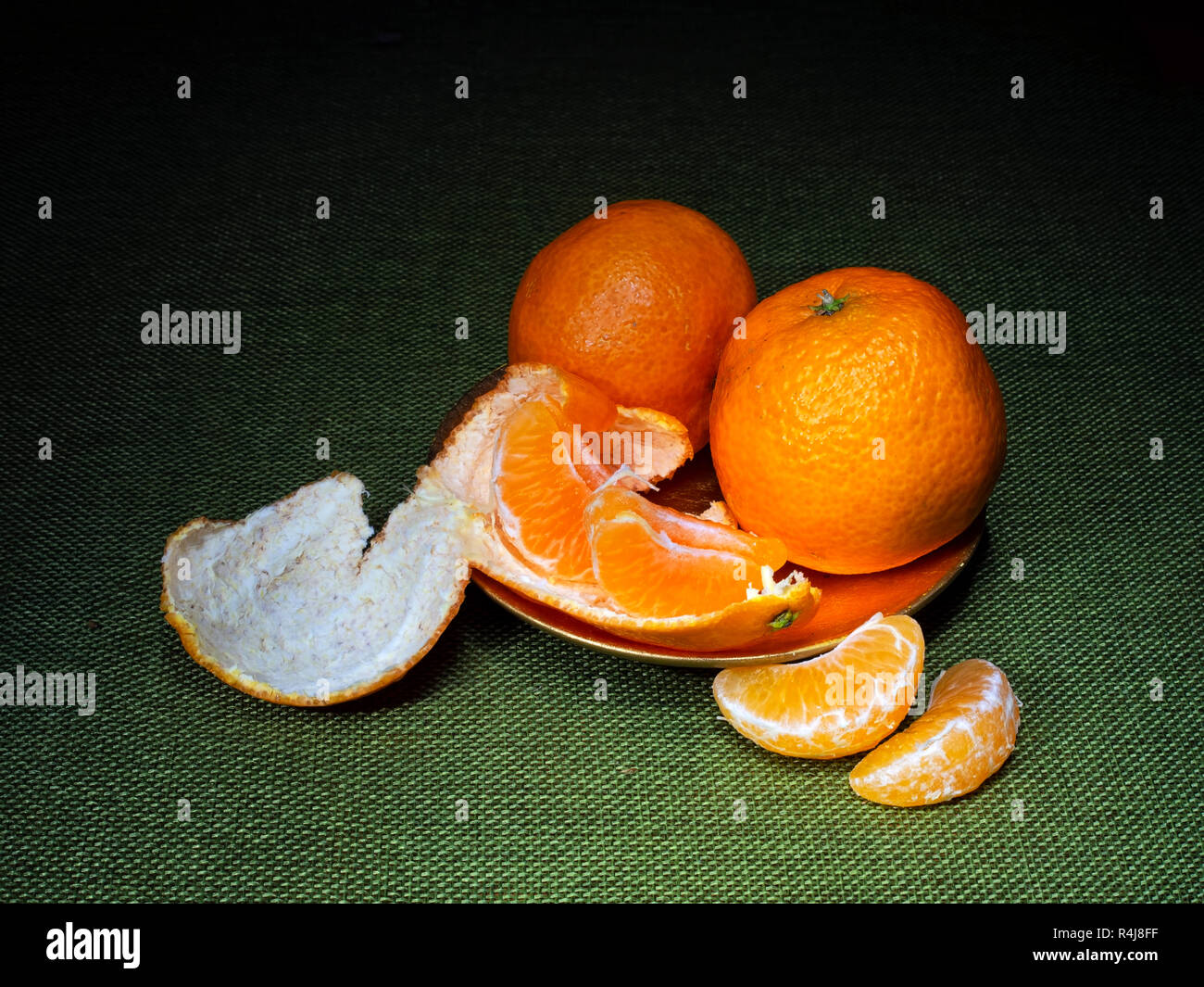 Mandarin o arance clementine, scuro ancora vita sul verde. Luce tecnica di pittura. Tre frutti, una parte sbucciata. Foto Stock