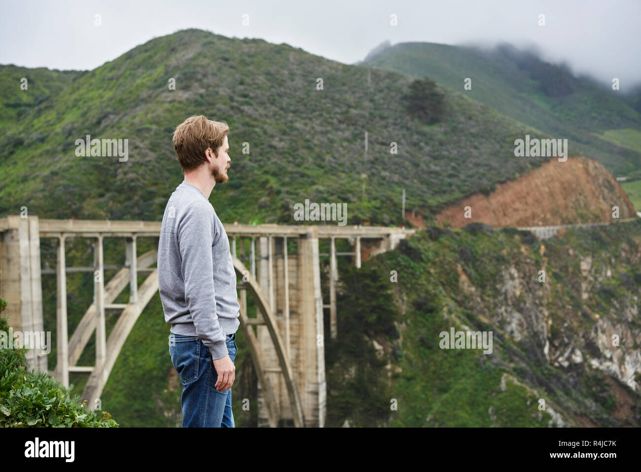 Uomo in piedi nella parte anteriore del ponte e montagne a Big Sur in California, Stati Uniti d'America Foto Stock