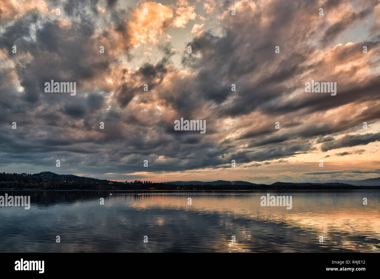 Nuvole scure al tramonto sul lago di Varese in un tranquillo paesaggio autunnale con colline all'orizzonte Foto Stock