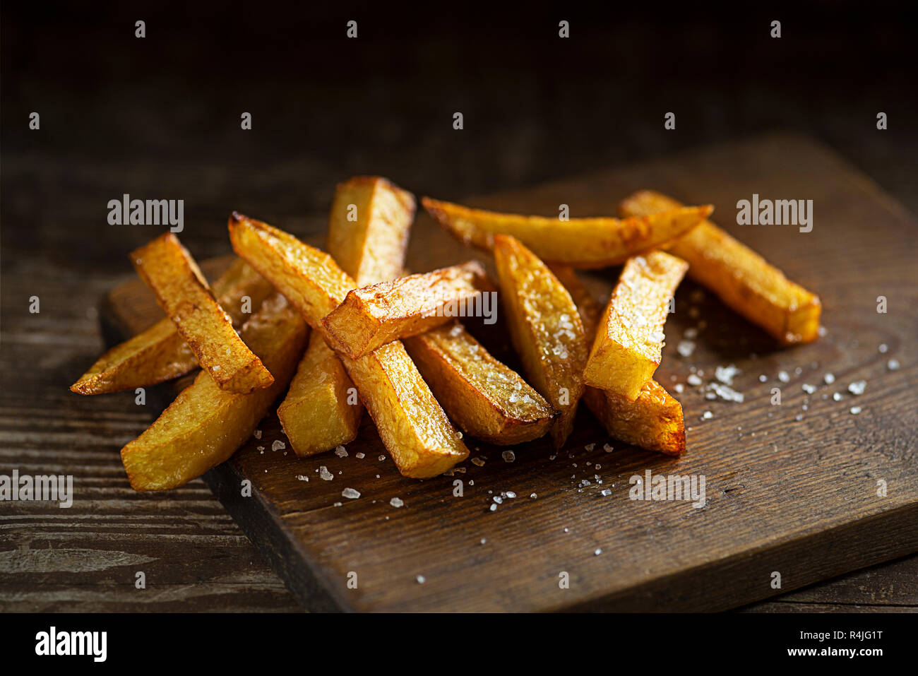 Delizioso il salato patatine fritte sul tavolo di legno e uno sfondo scuro Foto Stock