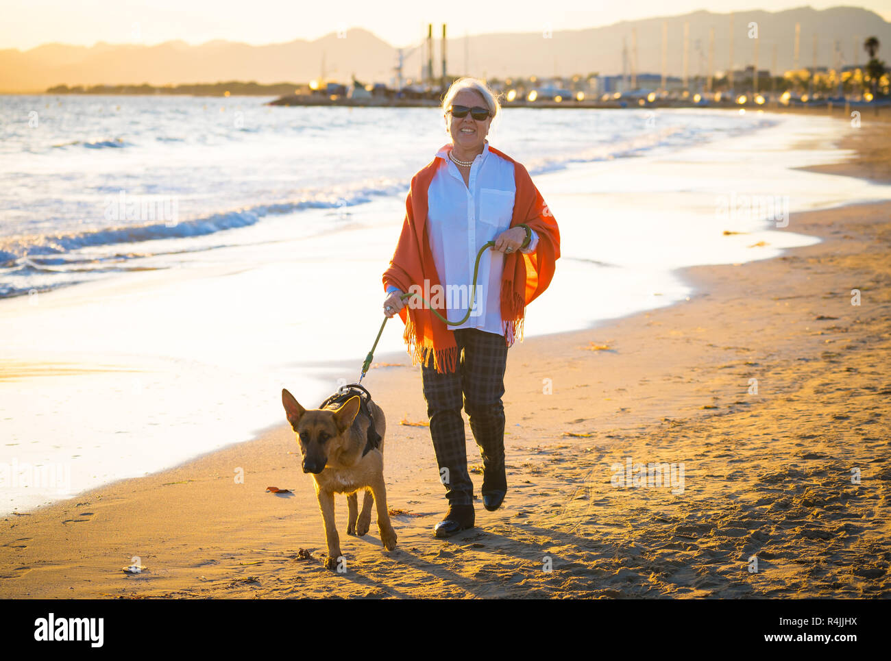 Pensione Bella donna più anziana e pet shepard tedesco cane a camminare lungo la riva mare sulla spiaggia in compagnia i vantaggi degli animali mantenendo activ Foto Stock